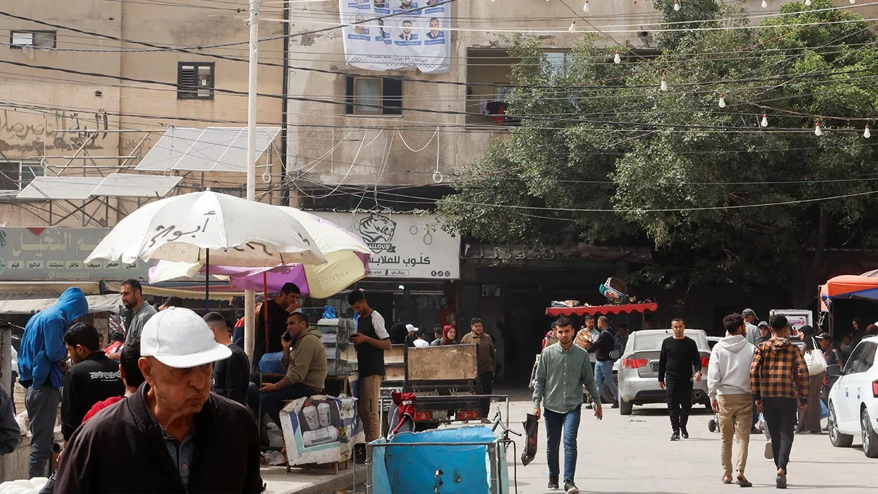 Palestinians walk past an electoral candidates list displayed in Deir al-Balah, central Gaza Strip, April 18, 2026. REUTERS/Haseeb Alwazeer