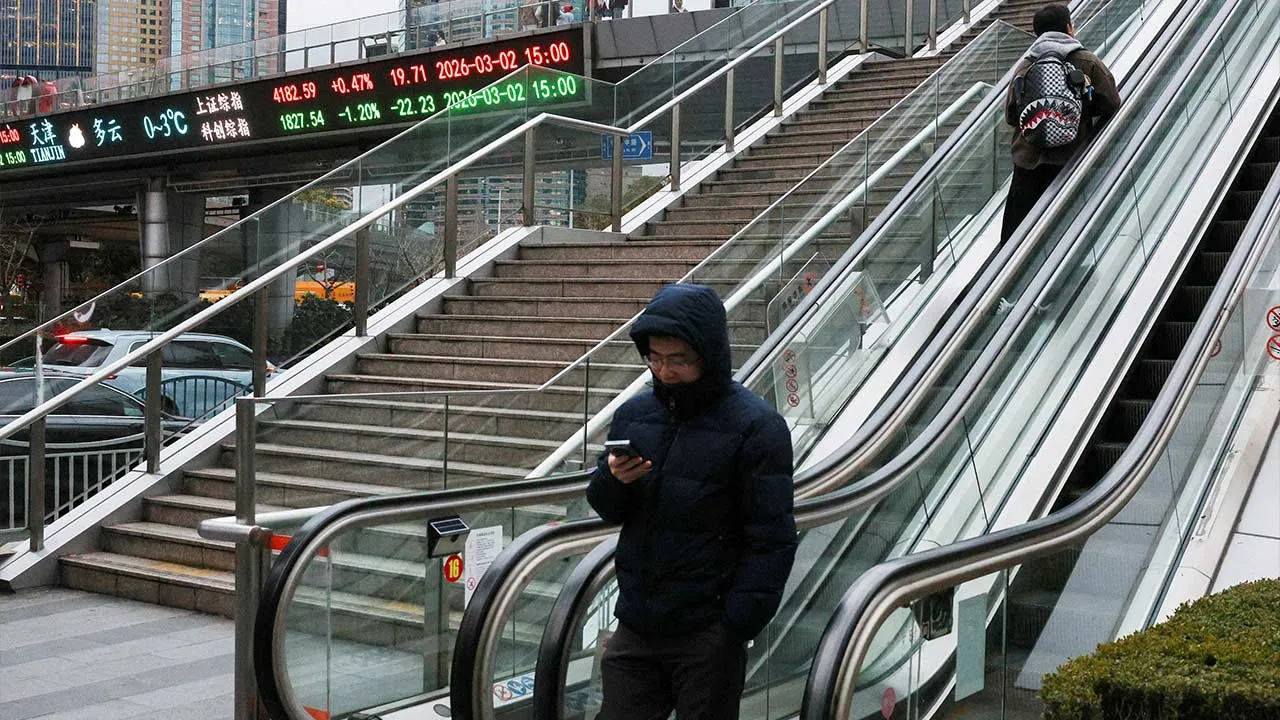 FILE PHOTO: An electronic board shows Shanghai stock indices as people ride an escalator on a pedestrian bridge in the Lujiazui financial district in Shanghai, China, March 2, 2026. REUTERS/Go Nakamura/File Photo