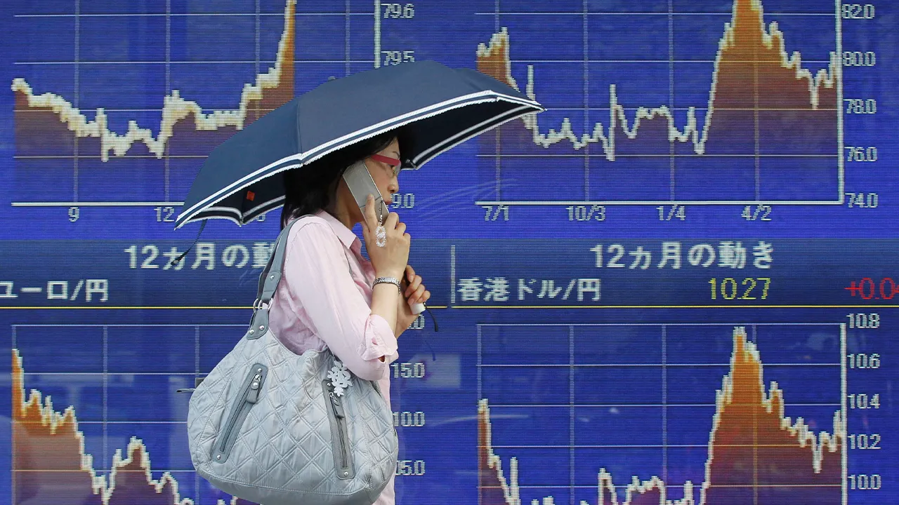 FILE PHOTO: A woman walks past an electronic board displaying major foreign currency rates against the Japanese yen outside a brokerage in Tokyo June 29, 2012. REUTERS/Yuriko Nakao/File Photo