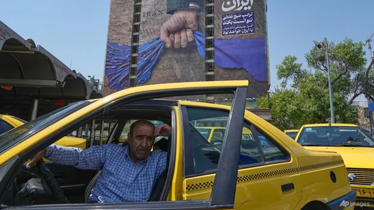 A taxi driver waits for passengers in front of a billboard that shows a graphic depicting a military personnel's hand holding the Strait of Hormuz in his fist with signs which read in Farsi: "In Iran's hands forever," "Trump couldn't do a damn thing," "The control of Strait of Hormuz will be Iran's forever," in Vanak Square in northern Tehran, Iran, Thursday, April 16, 2026. (AP Photo/Vahid Salemi)