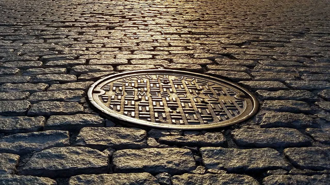 Sunlight shines on a manhole cover on a cobblestone street in New York City