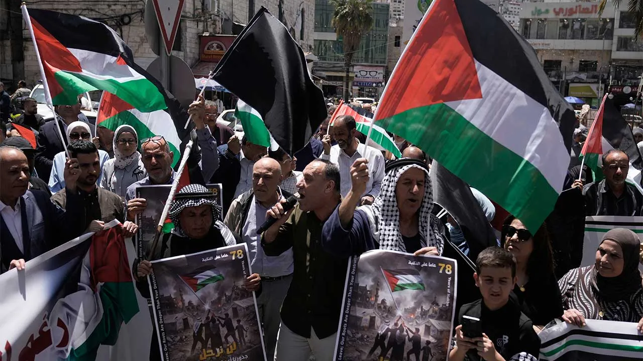 Palestinians wave their national flag in a rally ahead of the 78th anniversary of what they call the "Nakba," or "catastrophe", in the West Bank city of Nablus Monday, May 11, 2026. The Arabic writing reads "We will not leave; our roots are deeper than your destruction". (AP Photo/Majdi Mohammad)