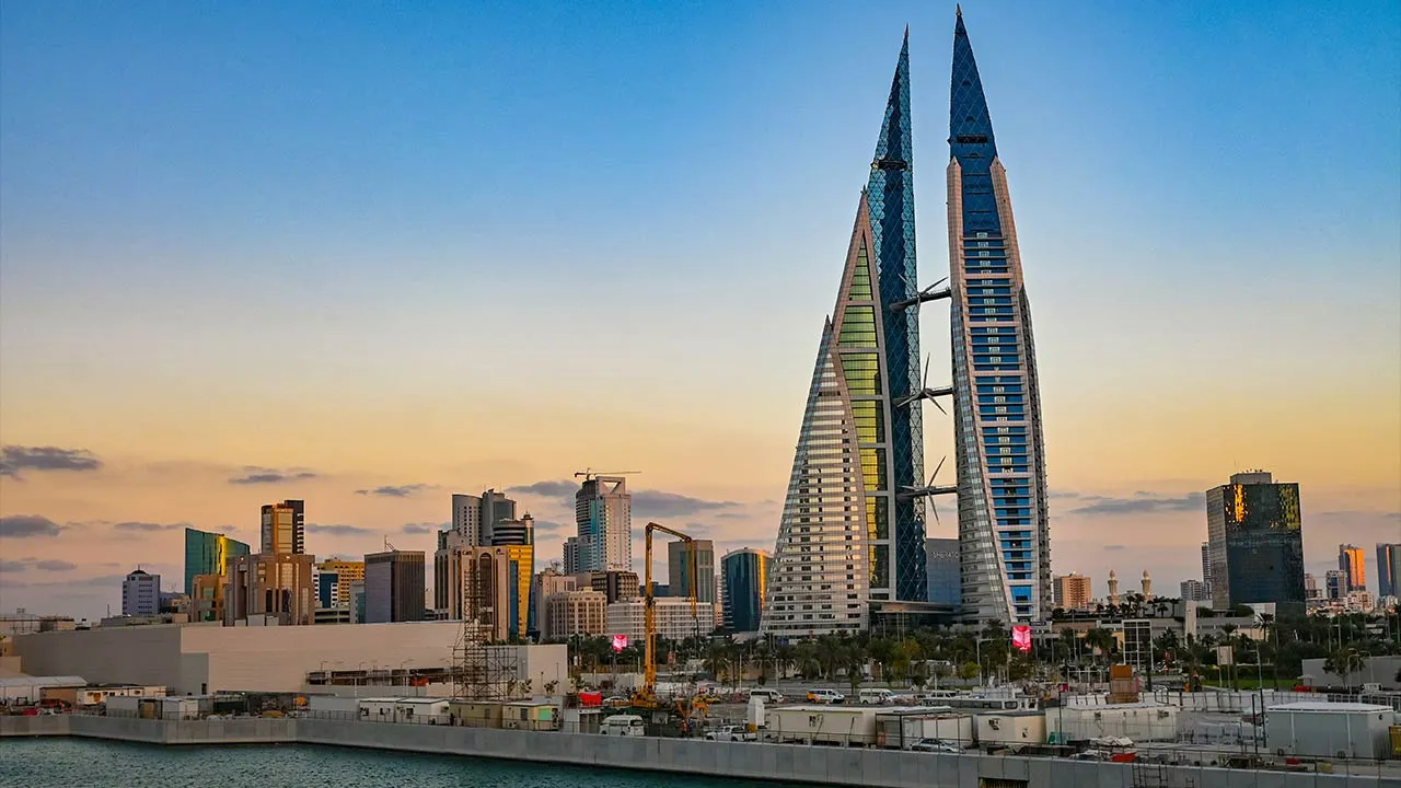 Modern skyline of Manama, Bahrain at sunset, featuring the iconic Bahrain World Trade Center with its wind turbines and futuristic architecture.