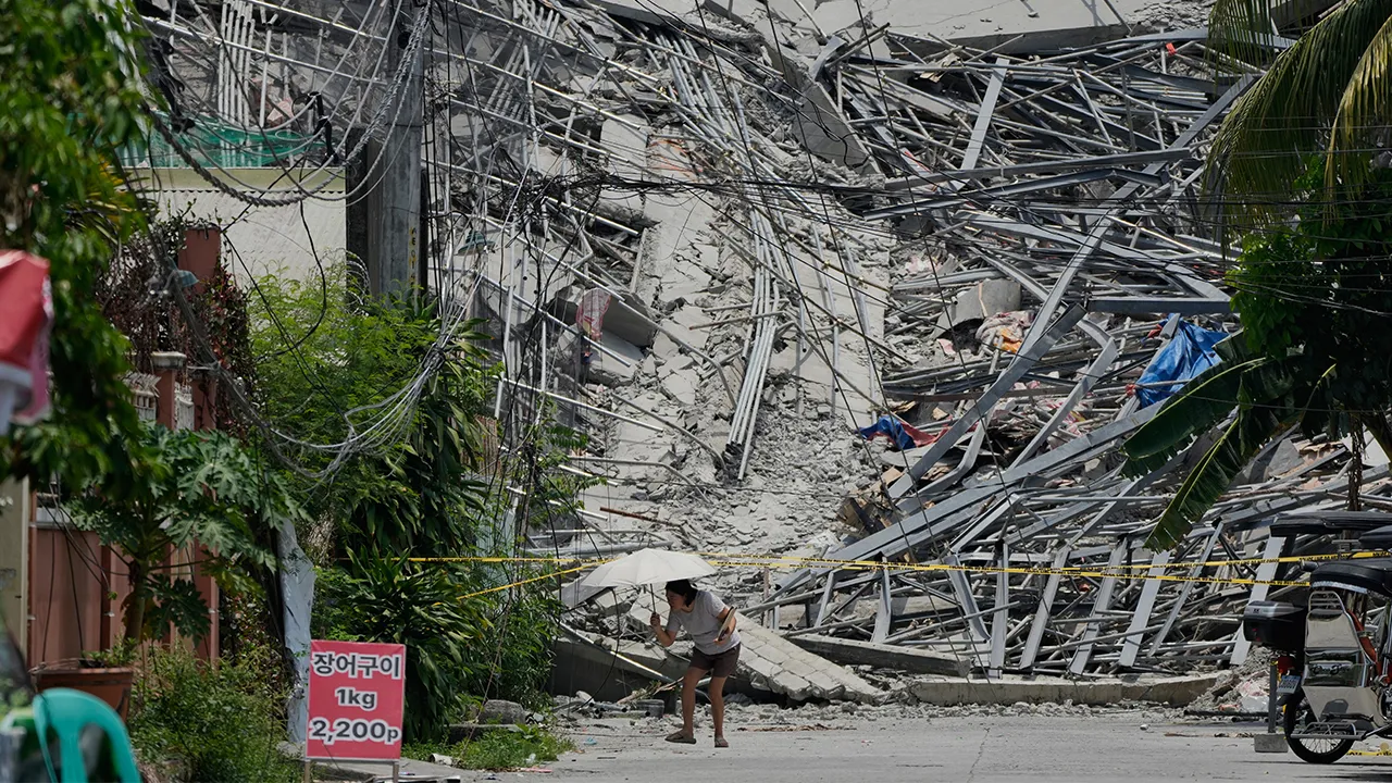 A woman walks beside a collapsed building where multiple people are believed to be trapped in Angeles city in Pampanga province, north of Manila Monday, May 25, 2026. (AP Photo/Aaron Favila)