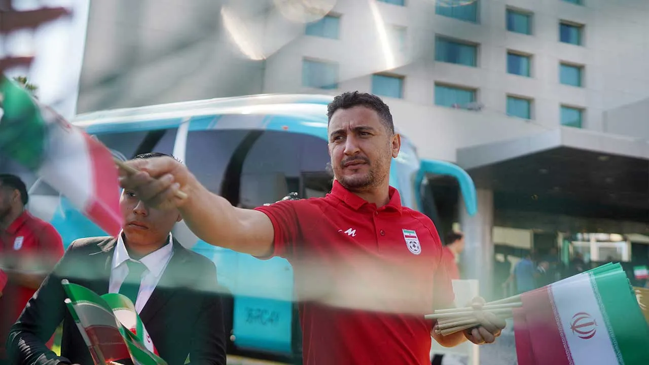 Soccer Football - FIFA World Cup 2026 - Iran leave Tijuana hotel ahead of first World Cup match - Tijuana, Mexico - June 14, 2026 An official gives out Iran flags to fans outside the hotel REUTERS/Victor Medina