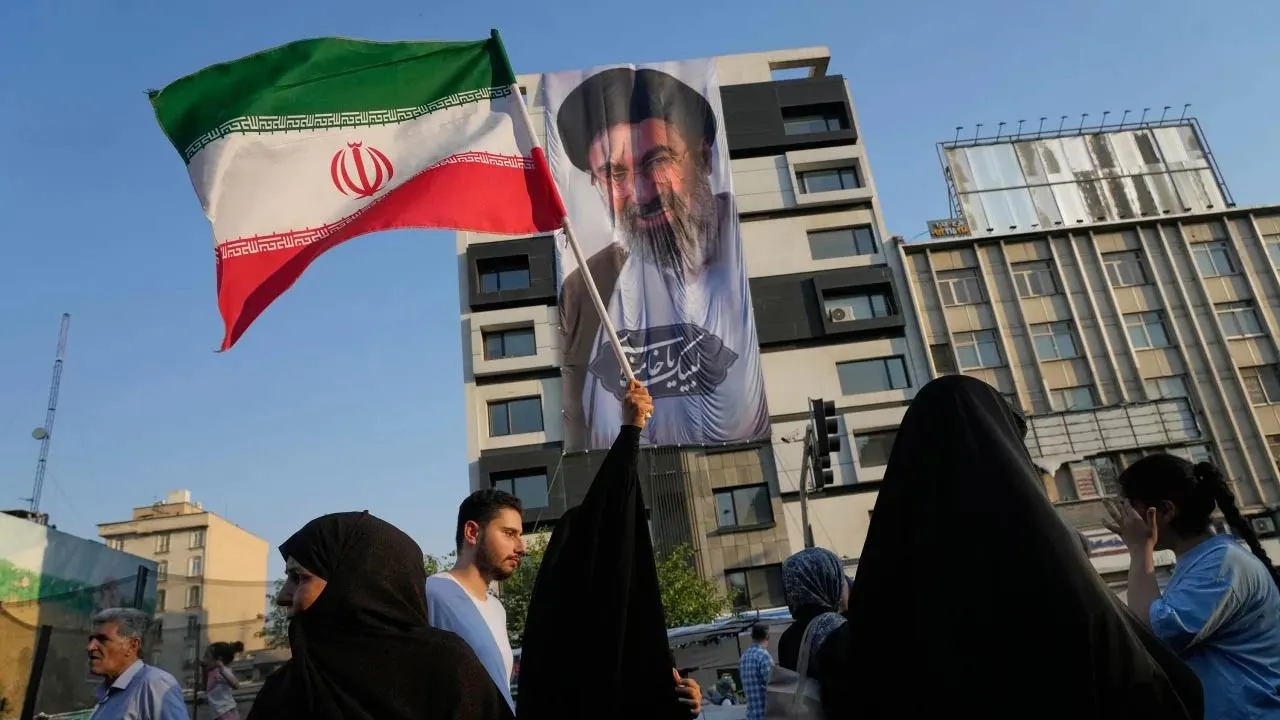 A woman holds up an Iranian flag in front of a banner showing the Supreme Leader Ayatollah Mojtaba Khamenei during a street festival celebrating Eid al-Ghadir, in Tehran, Iran, on Thursday, June 4. Vahid Salemi/AP