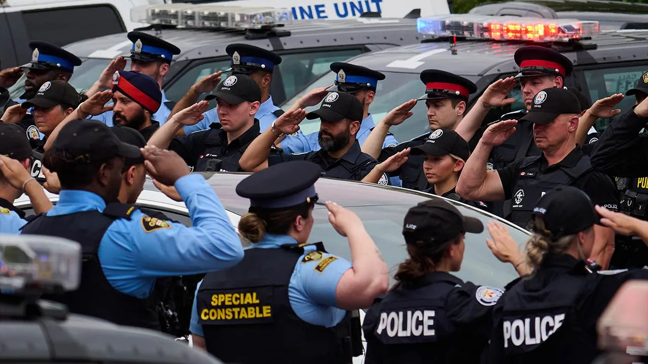 Police salute during a procession with the body of Toronto Police Const. Marc Pinizzotto, who was killed in the line of duty, at the Chief Coroner's office in Toronto, Thursday, June 11, 2026. (Sammy Kogan/The Canadian Press via AP)