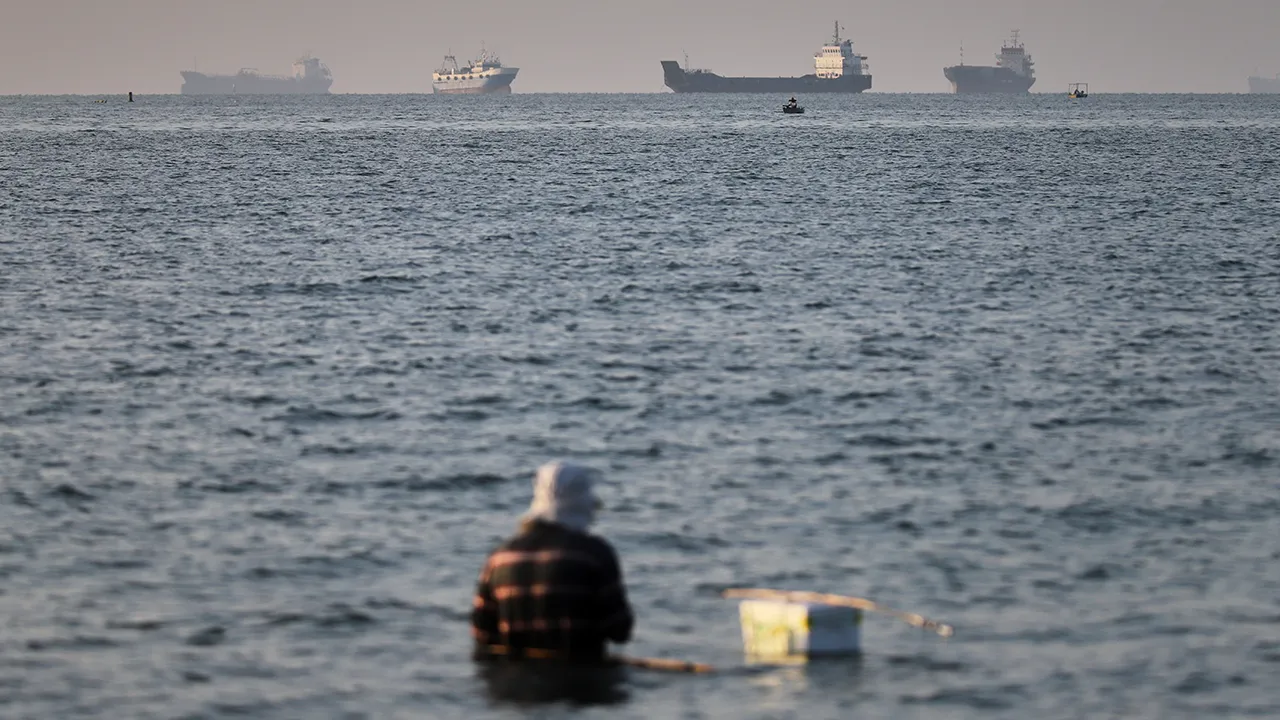 A person sits on shallow water as cargo and commercial vessels are anchored in the Strait of Hormuz off Bandar Abbas, Iran, Monday, June 8, 2026. (Amirhosein Khorgooi/ISNA via AP)