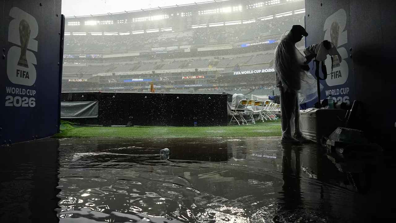 A photographer shelters from the rain as play is suspended during the World Cup Group I soccer match between France and Iraq in Philadelphia, Monday, June 22, 2026. (AP Photo/Petr David Josek)