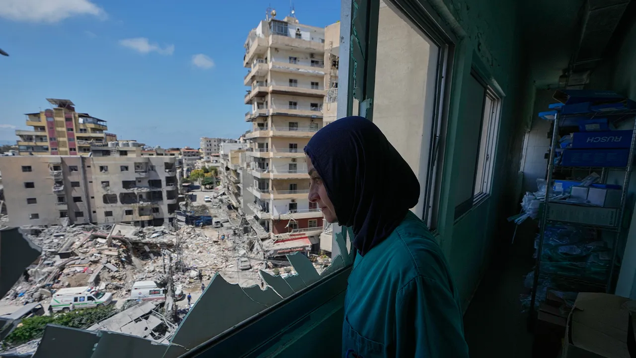 A nurse looks through a shattered window of the Jabal Amel Hospital into a destroyed building that was hit Monday in an Israeli airstrike, in the southern port city of Tyre, Lebanon, Tuesday, June 2, 2026. (AP Photo/Mohammed Zaatari)