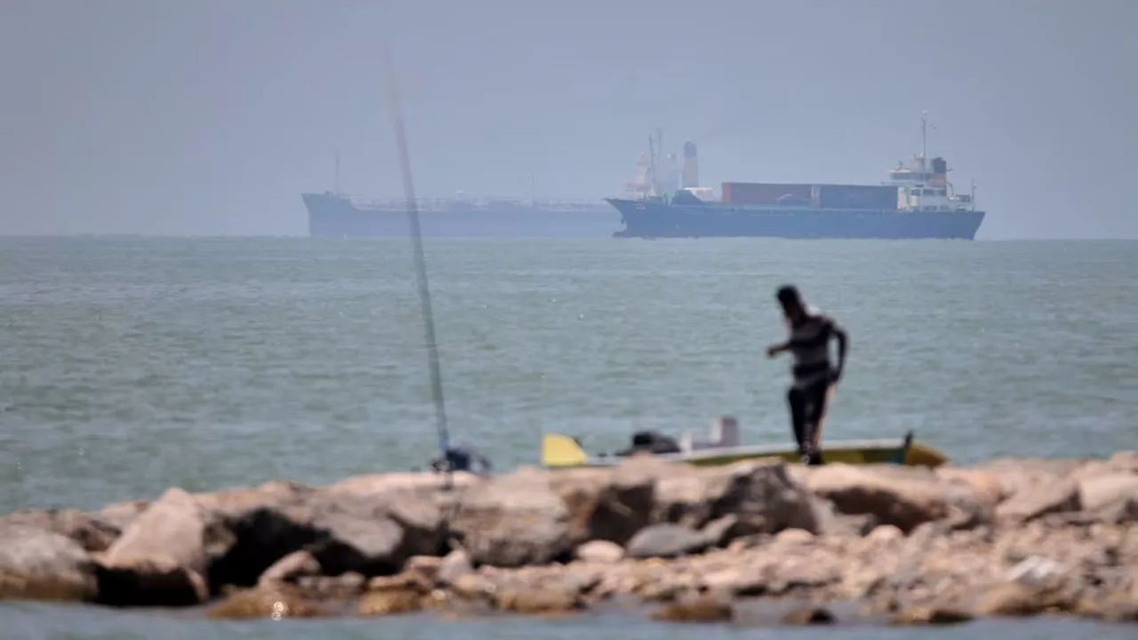A man stands beside a fishing pole along the shore as cargo ships and commercial vessels are seen in the Strait of Hormuz off Bandar Abbas, Iran, on June 17. Amirhosein Khorgooi/ISNA/AP