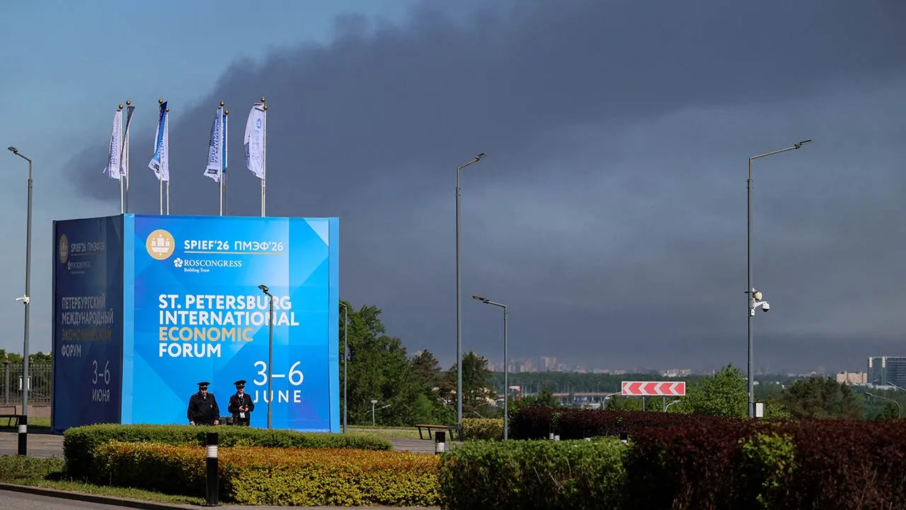 Police officers stand in front of a banner and flags with the logo of the St. Petersburg International Economic Forum (SPIEF) as heavy smoke billows in the background after Ukrainian drones hit infrastructure, according to the governor Alexander Beglov, in St Petersburg, Russia June 3, 2026. REUTERS/Stringer