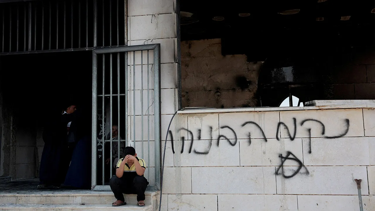 A Palestinian boy sits near a damaged a mosque, which Palestinians say was damaged by Israeli settlers, in Qusra near Nablus, in the Israeli-occupied West Bank, July 26, 2026. Graffiti on the wall reads "Revenge Benayahu", in reference to the 32-year-old Israeli reserve soldier Benayahu Mellet, who was killed in a shooting near the Palestinian village of Tal. REUTERS/Mohamad Torokman TPX IMAGES OF THE DAY