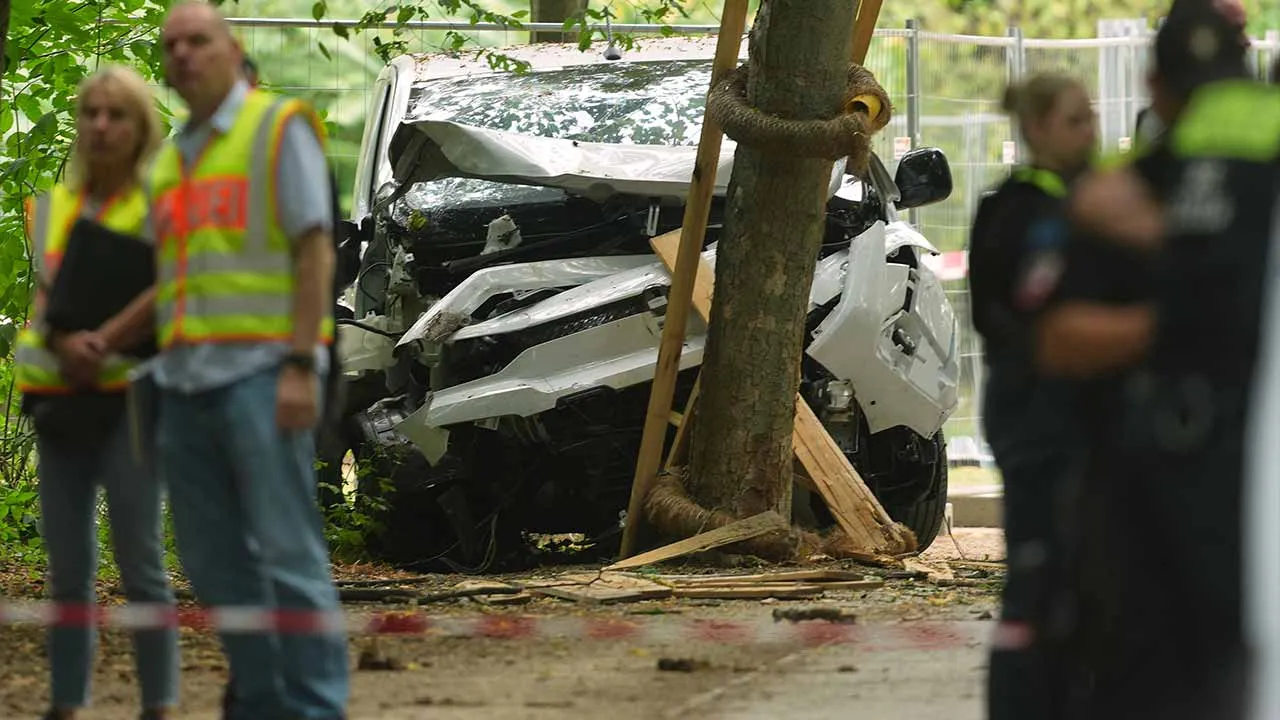 Police officers stand near a vehicle crashed into a tree after driving into a crowd near Berlin's annual Pride event, in Berlin, Germany, Sunday, July 26, 2026. (AP Photo/Markus Schreiber)