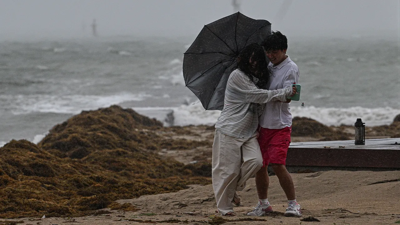 In this photo released by Xinhua News Agency, a tourist couple brace themselves against strong wind and rain at Tanmen central fishing port in Qionghai, south China's Hainan Province on Friday, July 3, 2026, as a severe weather system was affecting the area. (Pu Xiaoxu/Xinhua via AP)