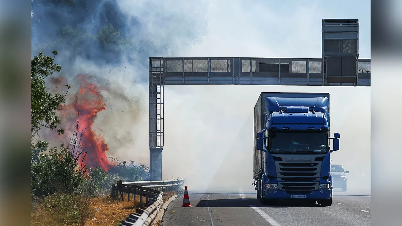 A truck drives next to a fire as a firefighting plane (not pictured) flies to battle wildfire near the A9 motorway near Beziers, France, July 3, 2026. REUTERS/Abdul Saboor