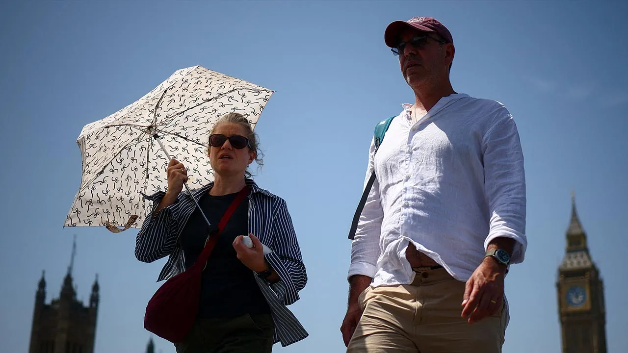 A woman uses an umbrella to shield herself from the sun as she walks on Westminster Bridge, near the Houses of Parliament, amid hot weather in London, Britain, June 23, 2026. REUTERS/Guglielmo Mangiapane