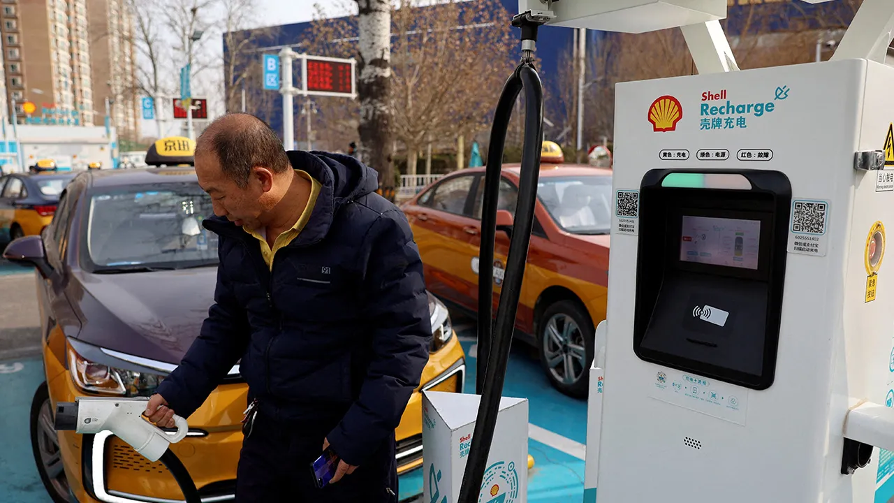 A man holds a charging plug to charge a taxi at a Shell electric vehicle (EV) charging station in Beijing, China February 2, 2024. REUTERS/Florence Lo