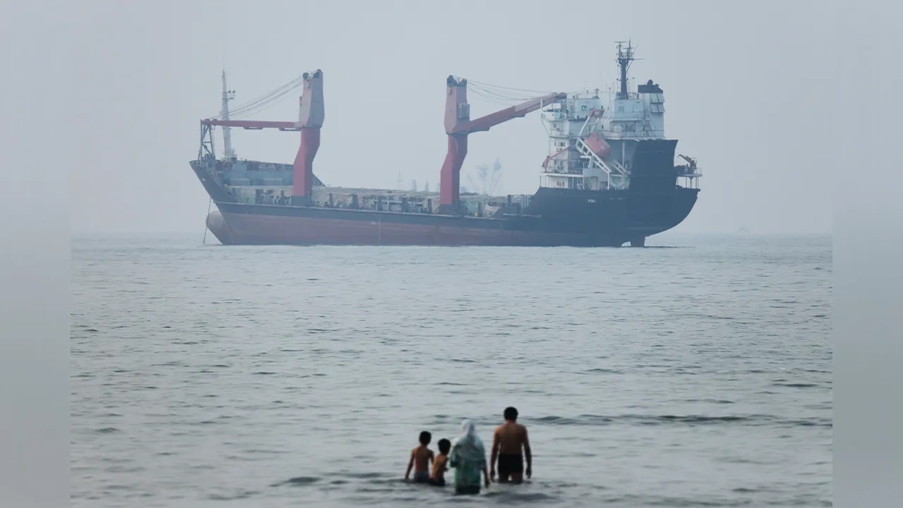 A group of people stands in shallow water as a cargo ship appears anchored in the Strait of Hormuz off Bandar Abbas, Iran, Tuesday, June 30, 2026. (Amirhosein Khorgooi/ISNA via AP)