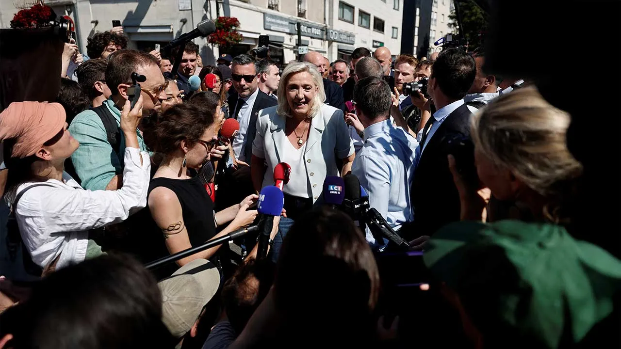 French far-right leader Marine Le Pen talks to journalists next to Jordan Bardella, president of the French far-right Rassemblement National (National Rally - RN) political party, as they arrive to visit a market in La Fleche, in the Sarthe department, a day after Le Pen announced her candidacy for the 2027 French presidential election following an appeals court ruling that shortened her ban on running for office while upholding her conviction for embezzling EU funds, France, July 8, 2026. REUTERS/Benoit Te