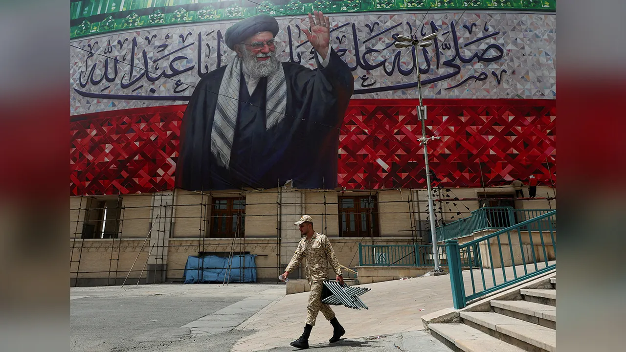 A member of the Basij paramilitary forces carries metal parts underneath a large banner depicting Iran's late Supreme Leader Ayatollah Ali Khamenei during preparations for a farewell ceremony for Iran's late Supreme Leader, who was killed on February 28 in Israeli and U.S. airstrikes, at the Imam Khomeini Grand Mosalla, in Tehran, Iran July 2, 2026. REUTERS/Mohammed Salem Foreign media in Iran operate under guidelines set by the Ministry of Culture and Islamic Guidance, which regulates press activity and pe