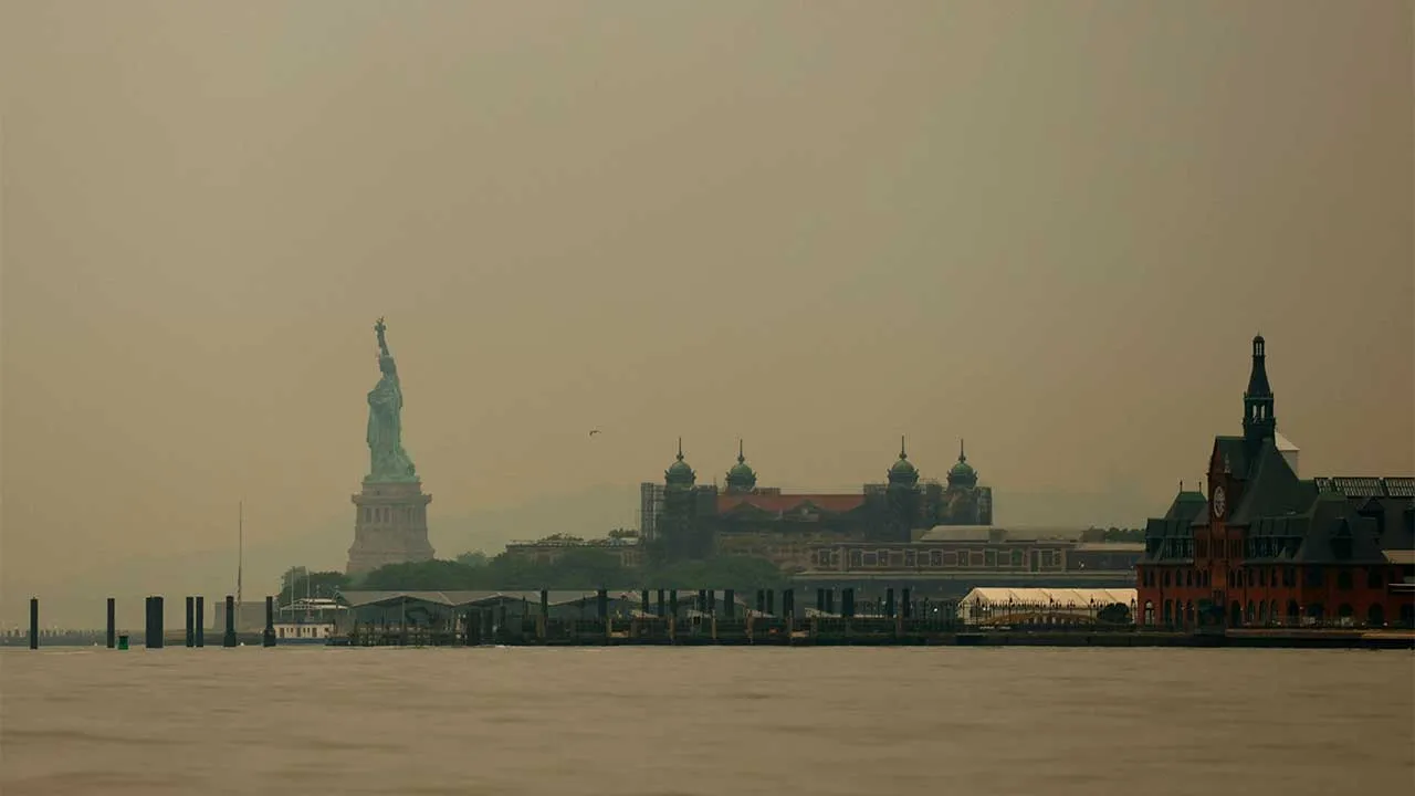 The Statue of Liberty and Ellis Island in Jersey City, New Jersey, are seen through a cover of wildfire smoke from New York Harbor, U.S., July 16, 2026. REUTERS/Mike Segar