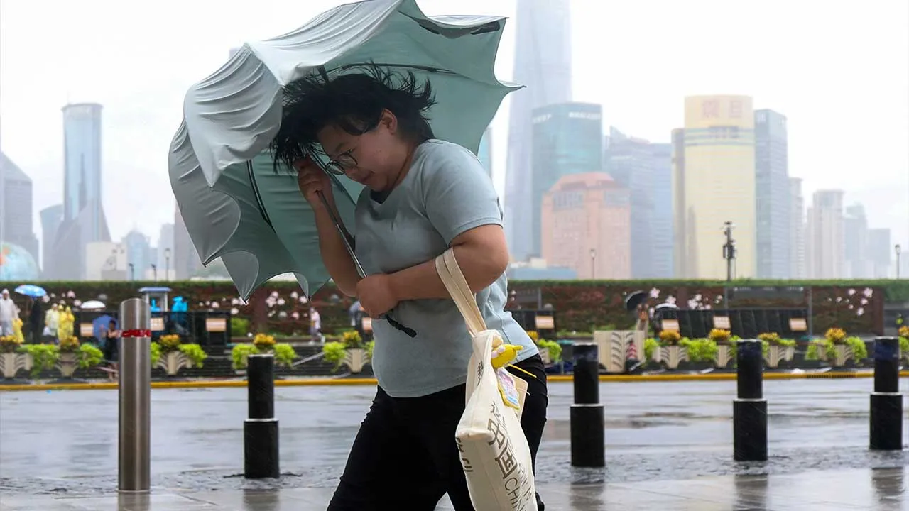 In this photo released by Xinhua News Agency, a woman struggles with her umbrella in strong wind and rain ahead of Typhoon Dolphin at Huangpu District of Shanghai on Sunday, Aug. 9, 2026.(Wang Xiang/Xinhua via AP)