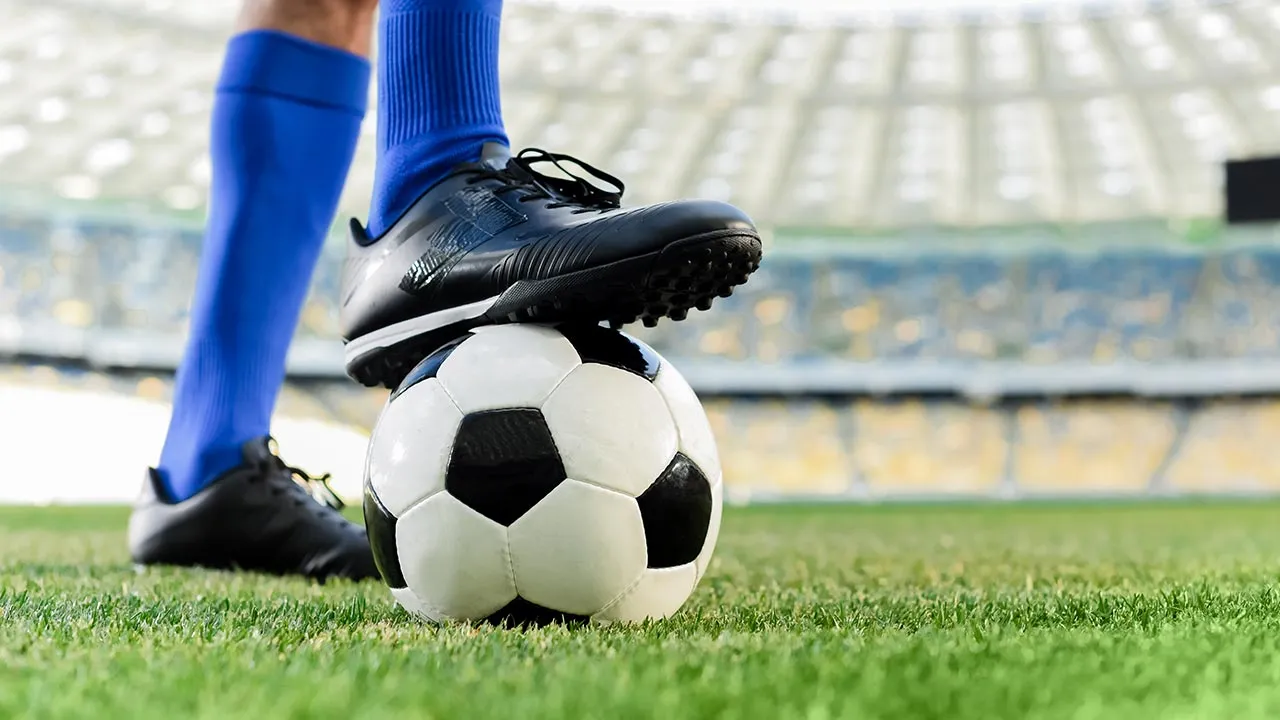 legs of professional soccer player in blue socks and soccer shoes on ball at stadium -- Adobe Stock