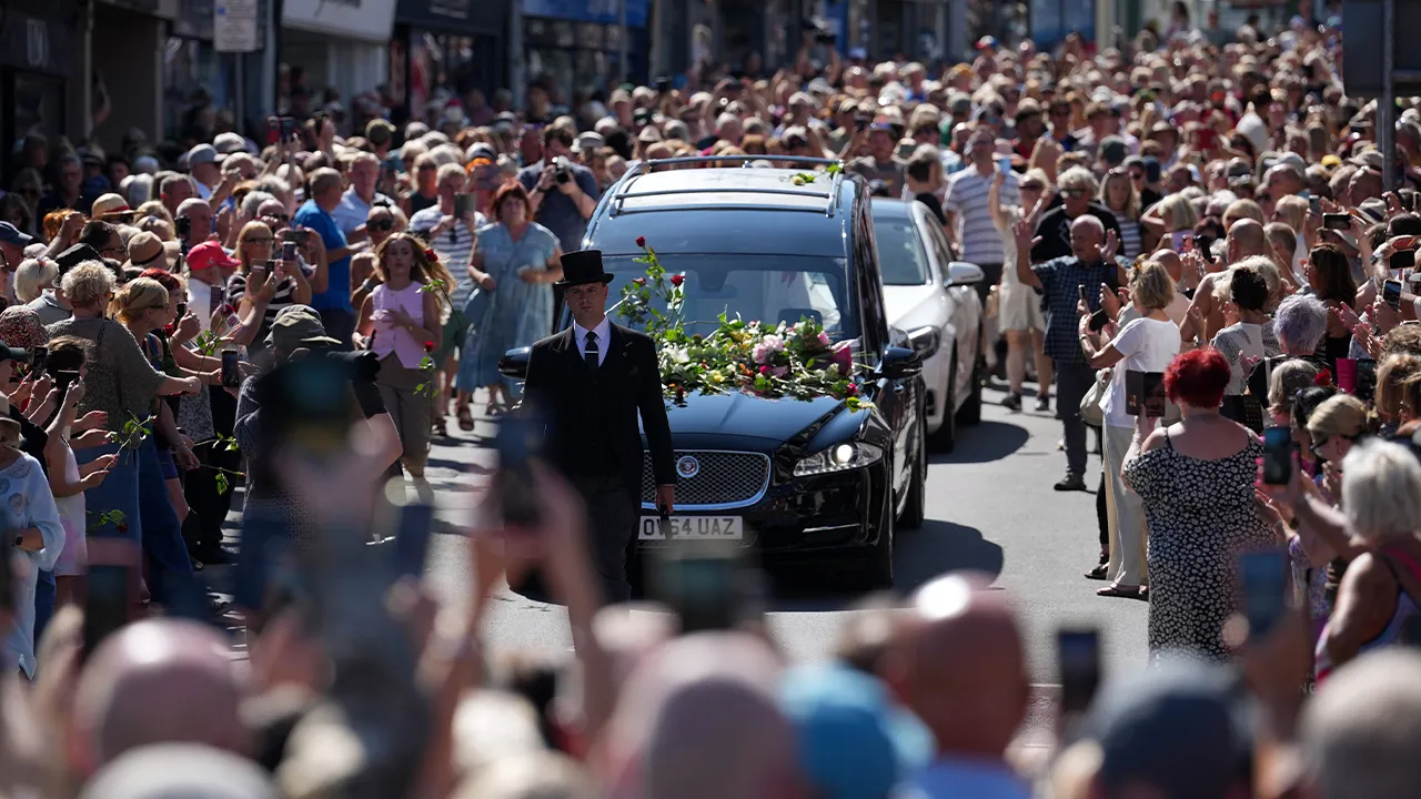 Fans of singer Bonnie Tyler line the streets as her coffin is transported in a hearse back to her former home ahead of her funeral, in Mumbles, Wales, Saturday, Aug. 15, 2026. (AP Photo/Alastair Grant)