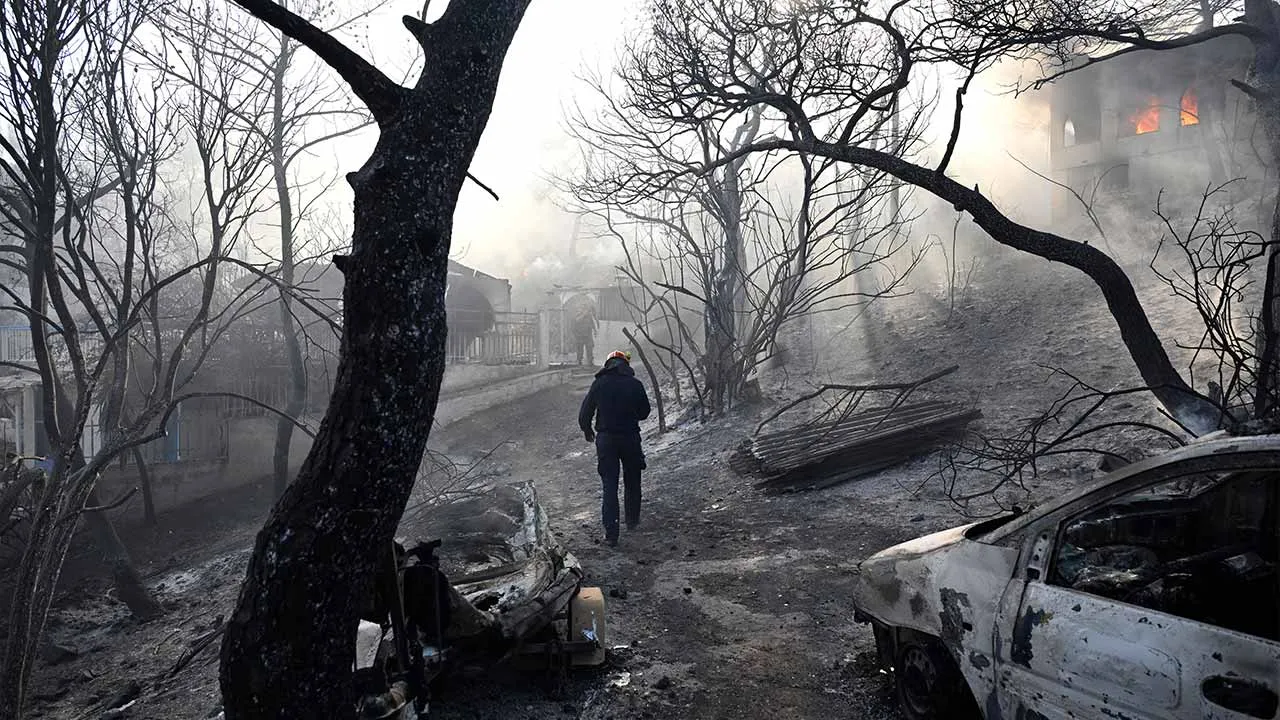 A firefighter walks through a burned area as flames engulf a house during a wildfire on the island of Salamina, west of Athens, Greece, Sunday, Aug. 16, 2026. (AP Photo/Michael Varaklas)