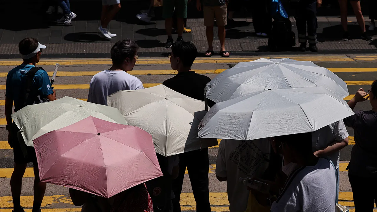 Pedestrians hold umbrellas as they wait to cross a street amid a heatwave, in Hong Kong, China, August 10, 2026. REUTERS/Tyrone Siu