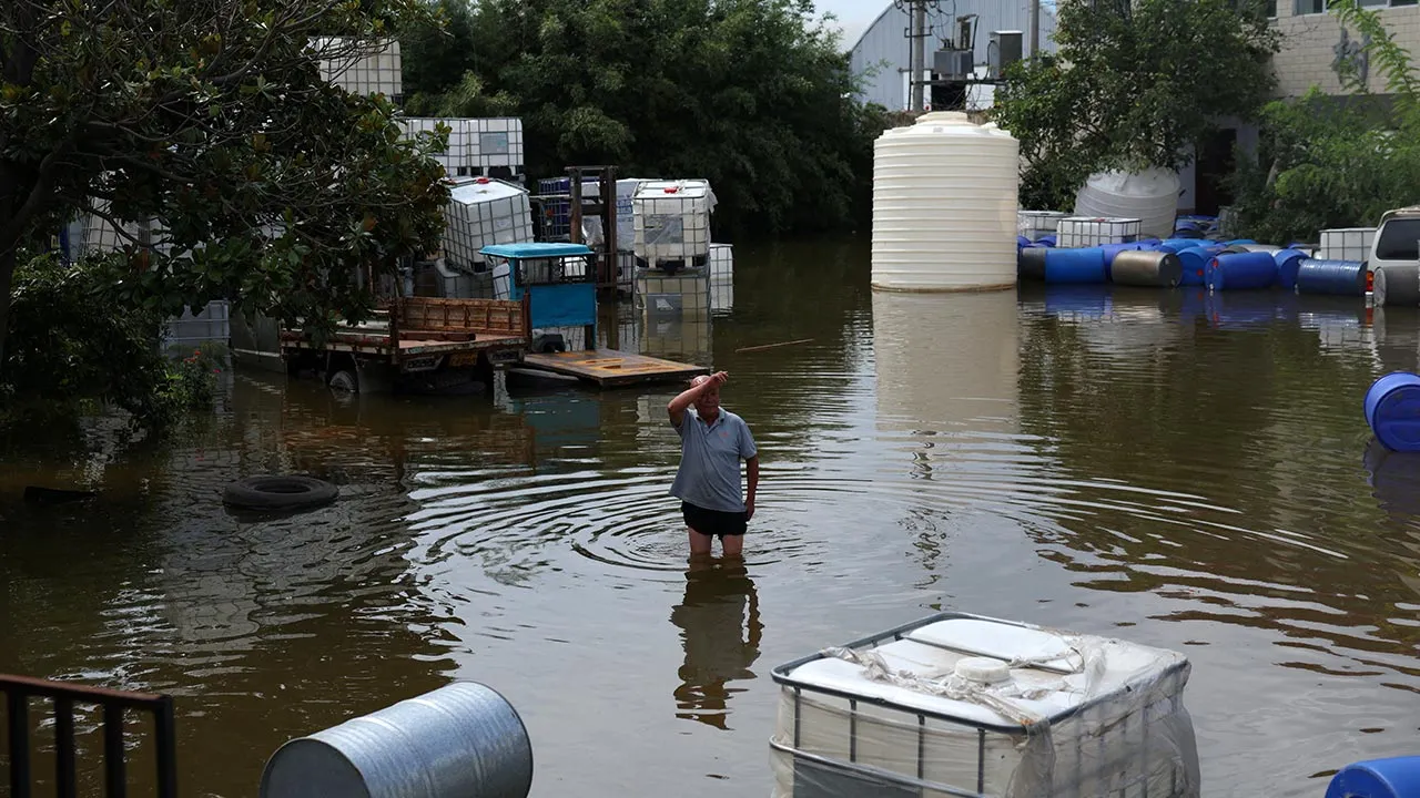 A man wades through floodwaters at a construction material storage yard, following heavy rainfall brought by remnants of Typhoon Dolphin, in Xuchang, Henan province, China August 13, 2026. REUTERS/Tingshu Wang