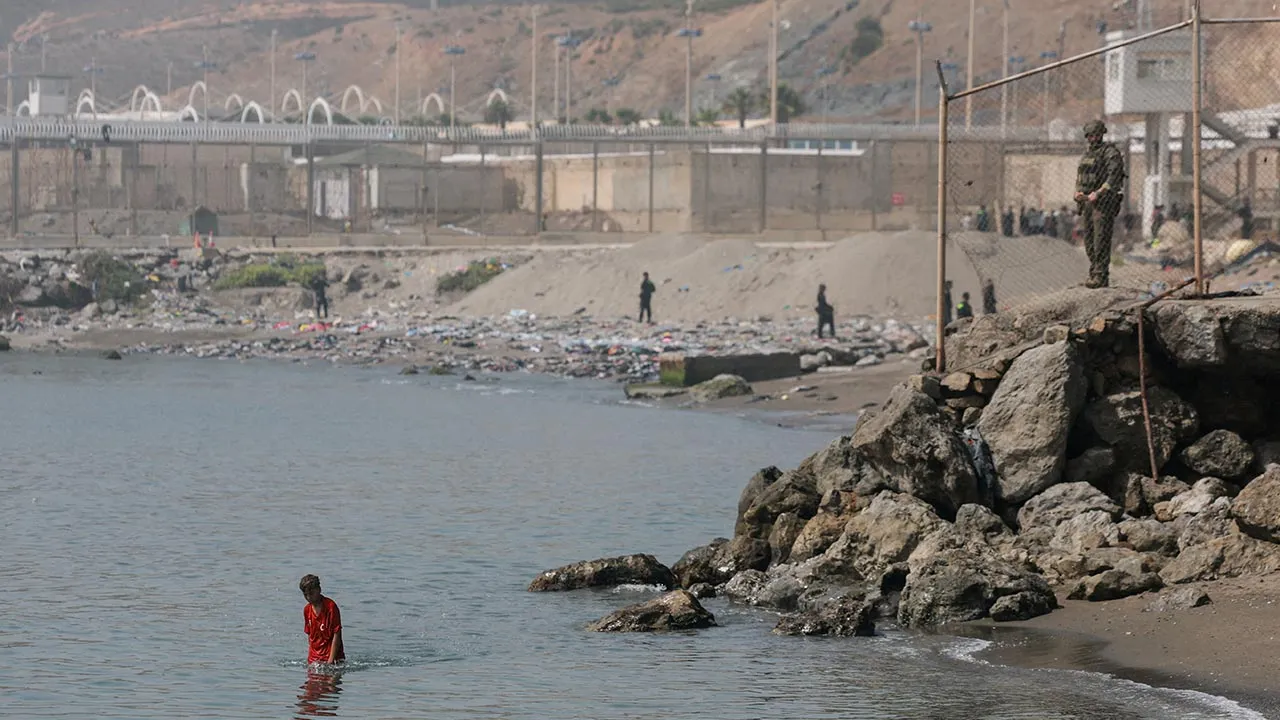 A member of the Spanish security forces stand guard as a migrant minor from Morocco walks in the water after crossing into Ceuta by sea, amid recent mass crossings of migrants on foot and by sea from Morocco into Spanish territory, in Ceuta, Spain, August 1, 2026. REUTERS/Violeta Santos Moura