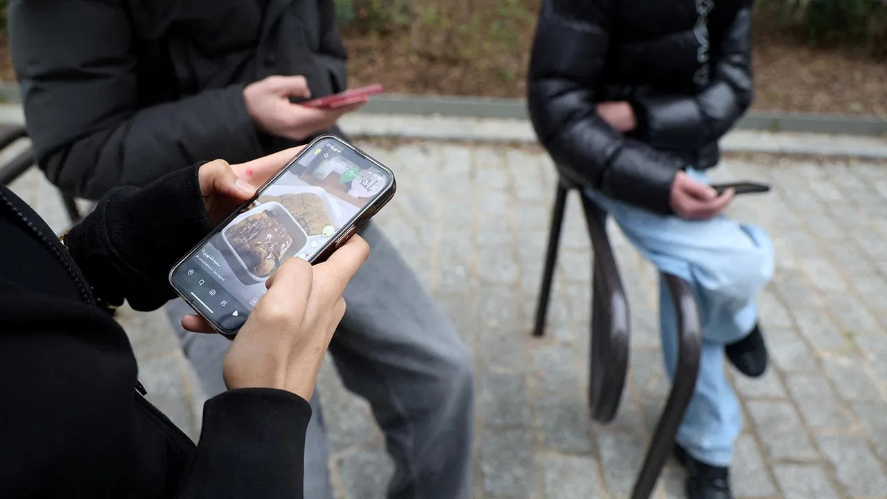 FILE PHOTO: Teenagers look at their mobile phone screens during an interview with Reuters about the bill aimed at banning the use of social networks for those under 15 and mobile phones in high schools from the start of the 2026 school year, in Paris, France, February 20, 2026. REUTERS/Manuel Ausloos/File Photo