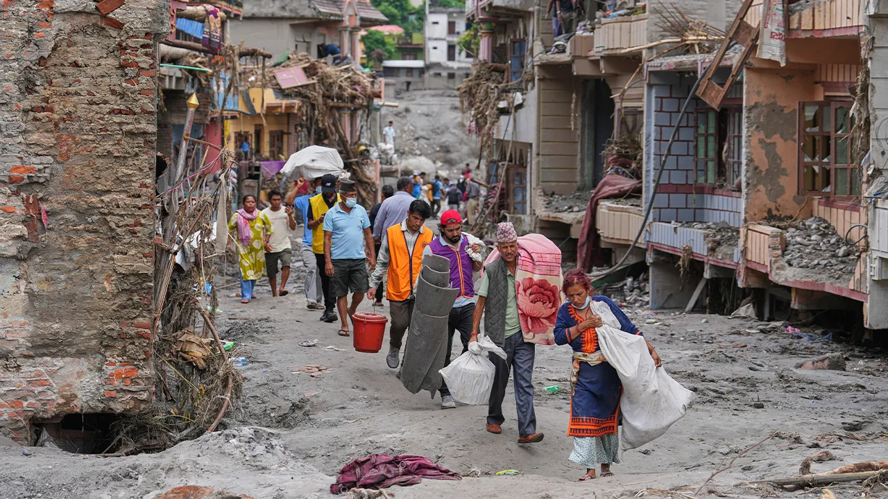 Residents carry their belongings salvaged from their damaged homes filled with mud and debris in Devighat, in Nepal's Nuwakot district, Saturday, Aug. 29, 2026, following the Aug. 26 flash floods. (AP Photo/Rajesh Kumar Singh)