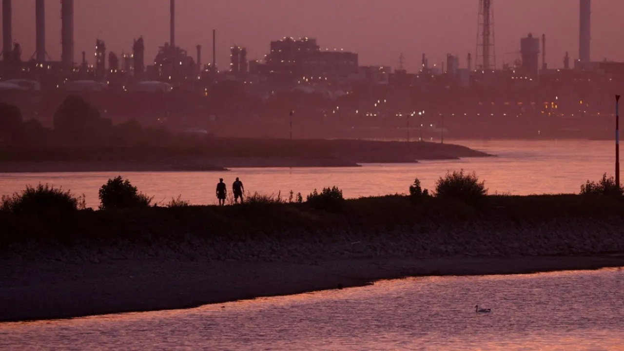 People walk on a strip of land between the Hitdorf yacht harbour basin and the Rhine River, with the Dormagen Chempark site in the background, at low water levels, before sunset in Leverkusen, Germany, August 3, 2026. REUTERS