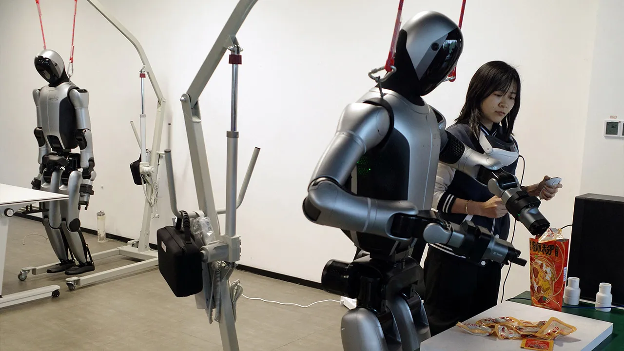 A human trainer teaches a robot how to package noodles while holding a controller and wearing a headset fitted with motion sensors at a robot data training center in Liuzhou, Guangxi, China April 22, 2026. REUTERS/Laurie Chen