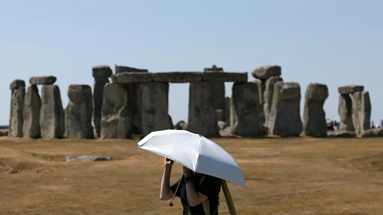 A visitor uses an umbrella to shield from the sun as she walks around Stonehenge, an ancient stone circle, after Britain’s Environment Agency declared over 70% of England to be in drought, and with an extreme heat warning in place for Thursday, near Amesbury, Britain, August 13, 2026. REUTERS/Toby Melville