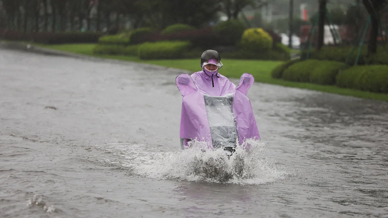 A person rides an electric scooter through a flooded road after heavy rain brought by Typhoon Bavi in Wenzhou, Zhejiang province, China July 12, 2026. REUTERS/Go Nakamura 