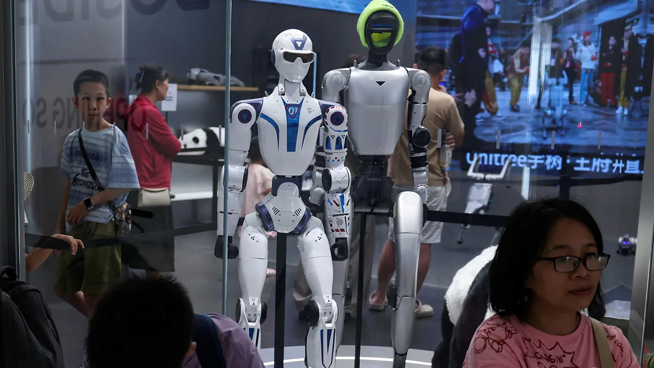 People sit near Unitree's G1 and R1 humanoid robots on display at a Unitree store in Beijing, China August 10, 2026. REUTERS/Tingshu Wang