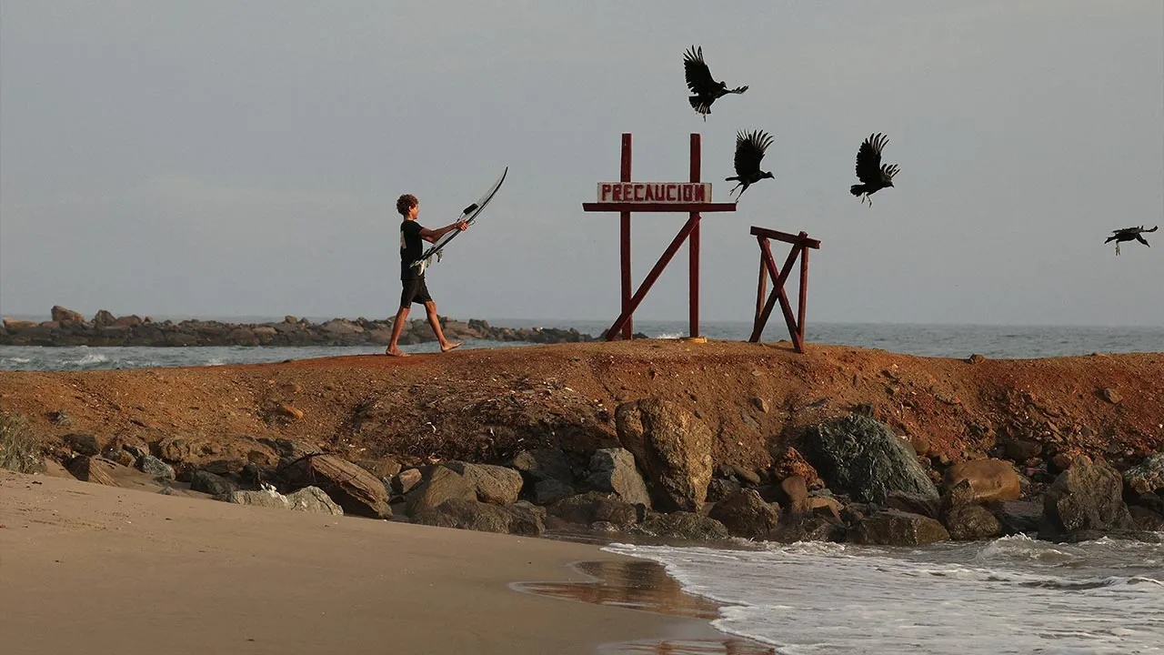 A boy carries a surfboard before a “Paddle Out” memorial ceremony honoring people who died in the June 24 earthquakes, off the coast of Catia La Mar, La Guaira, Venezuela, August 1, 2026. REUTERS/Gaby Oraa REFILE - ADDING BYLINE