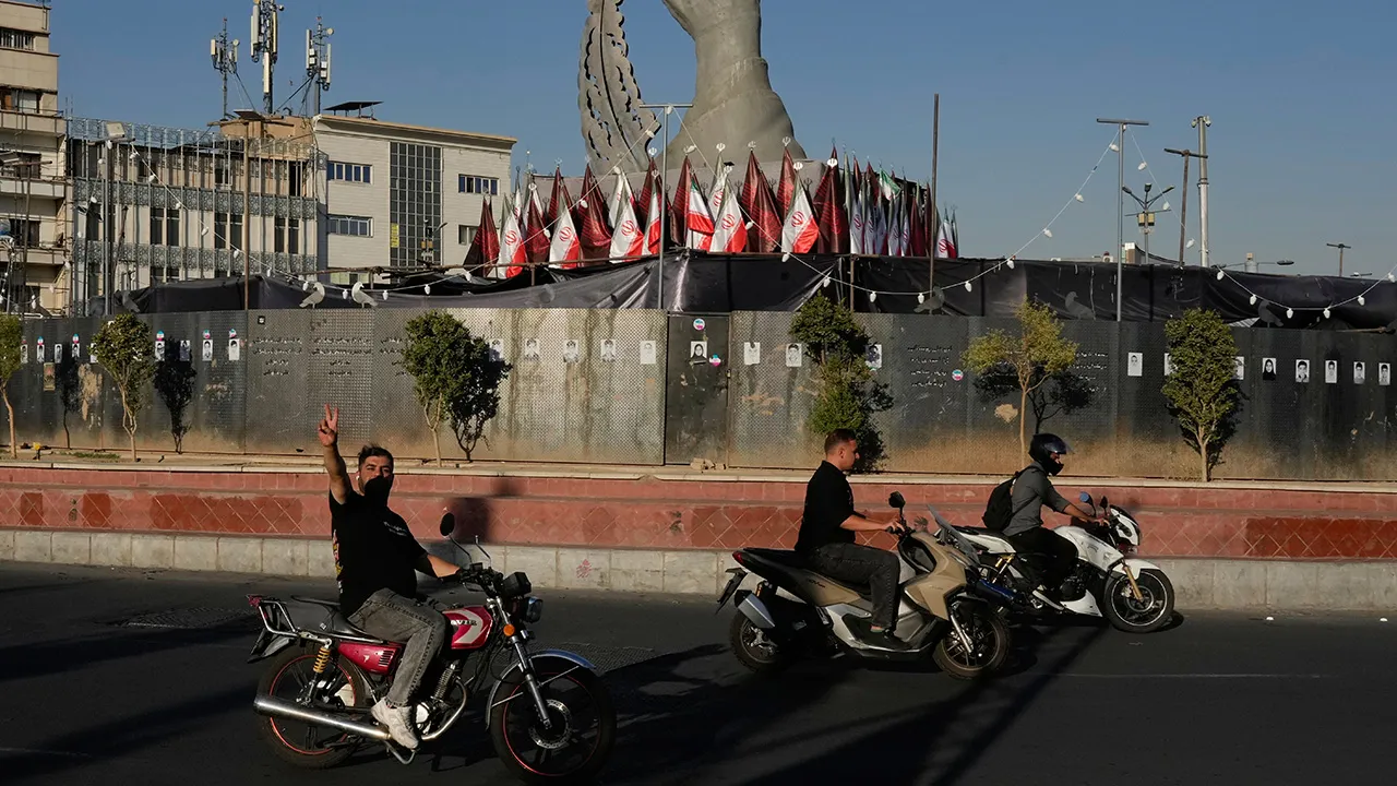 A man reacts to the camera while driving past a monument depicting the clenched fist of the late Iranian Supreme Leader Ayatollah Ali Khamenei, who was killed in the U.S. and Israel strike on Feb. 28, and a missile at the Islamic Revolution square in downtown Tehran, Iran, Tuesday, Sept. 15, 2026. (AP Photo/Vahid Salemi)