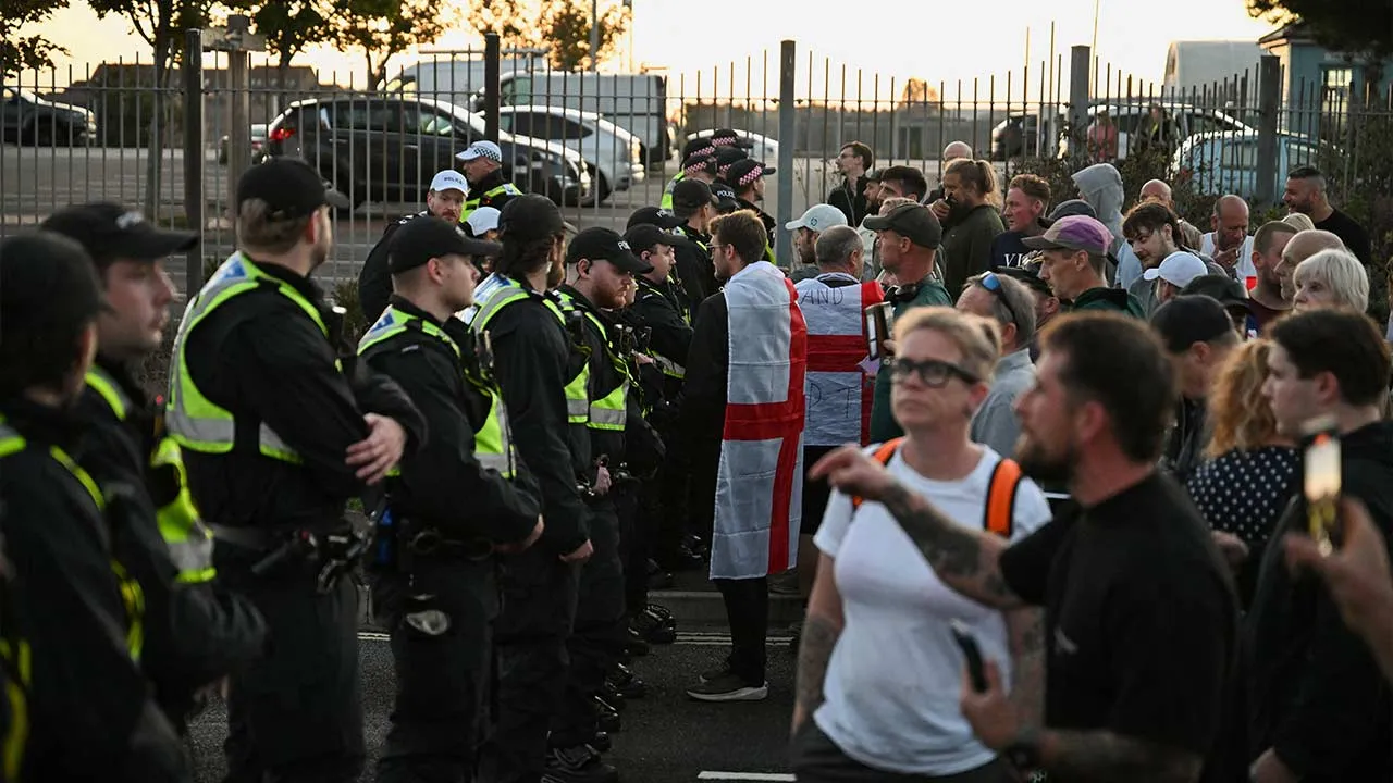 Demonstrators wearing flags of England stand facing police officers as people gather during a protest linked to the arrival of a migrant boat, in Gosport, Britain, September 22, 2026. REUTERS/Chris J. Ratcliffe
