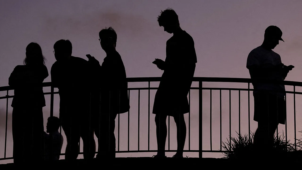FILE PHOTO: People use their mobile phones, ahead of new law banning social media for users under 16 in Australia, at dusk in Brisbane, Australia, December 8, 2025. REUTERS/Hollie Adams/File Photo