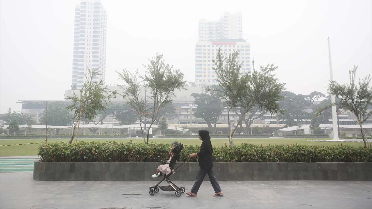 A woman pushes a stroller in a park as haze from wildfires shrouds the city of Medan, North Sumatra, Indonesia, Thursday, Oct. 15, 2026. (AP Photo/Binsar Bakkara)