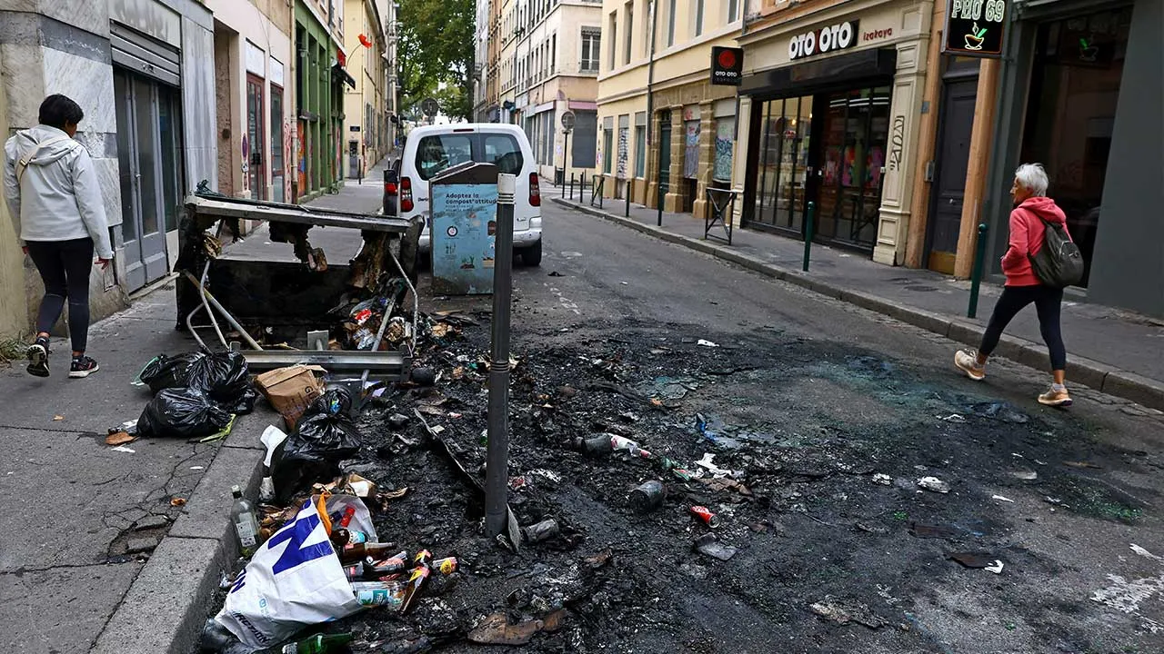 People walk past burnt debris on the side of a street, the day after clashes during a second day of nationwide protests against the cost of living and rising fuel prices, in Lyon, France, October 25, 2026. REUTERS/Lisi Niesner