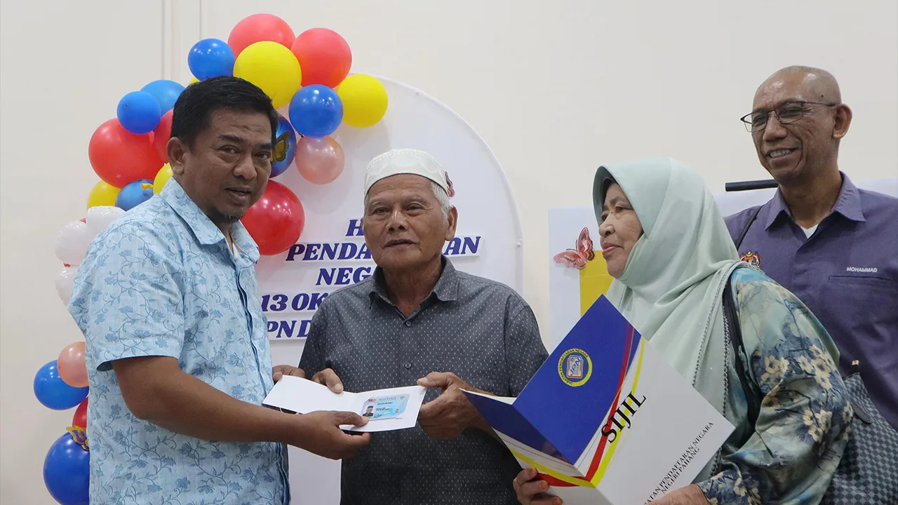PEKAN, 13 Okt - Ketua Pengarah Jabatan Pendaftaran Negara (JPN), Datuk Badrul Hisham Alias (kiri) menyerahkan MyKad generasi baharu kepada warga emas, Pahang Awang Mohamad, 74, (dua, kiri) yang ditemani isterinya, Fuziah Ibrahim, 71, (dua, kanan) pada Program Literasi Pendaftaran di Pejabat JPN Pekan, hari ini._BERNAMA