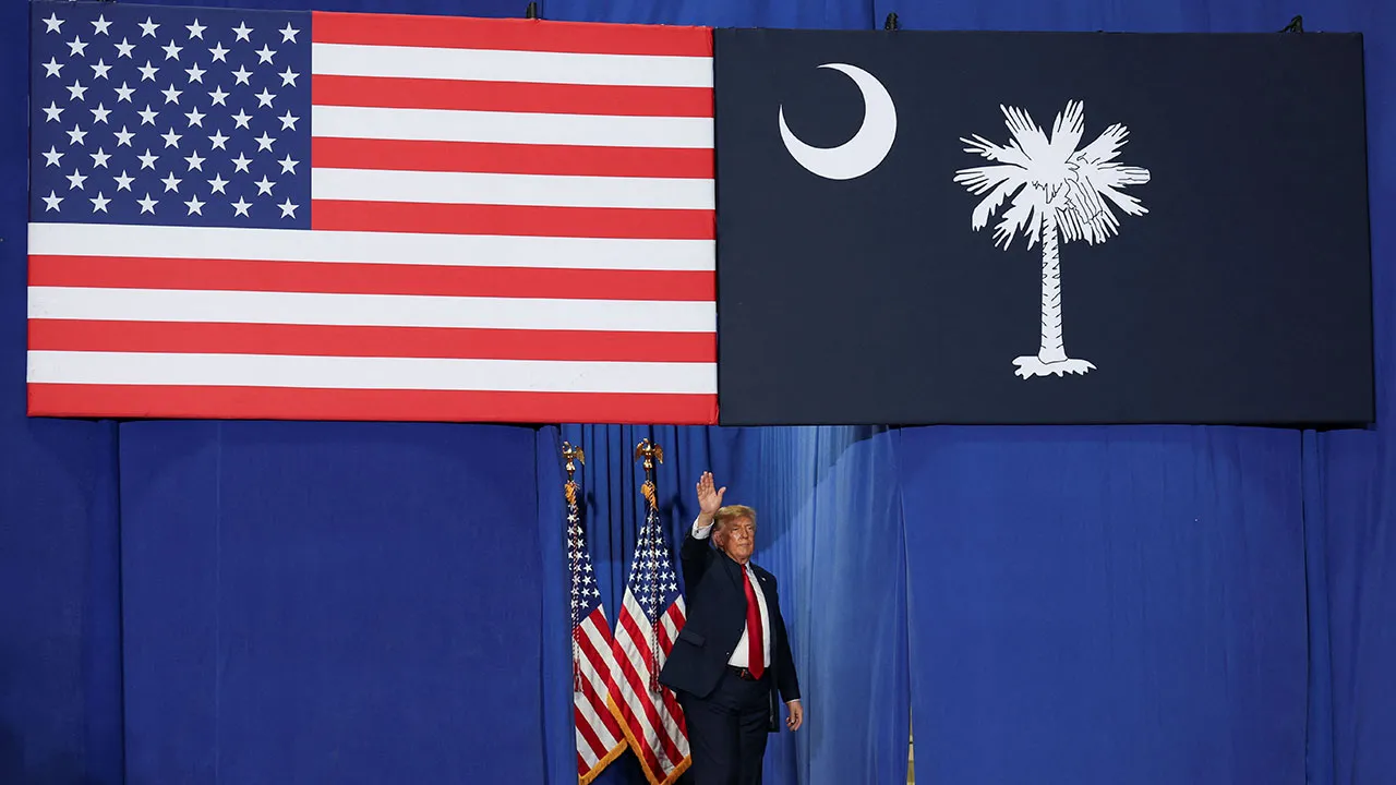 US President Donald Trump waves from beneath the US and South Carolina flags at a rally in support of Republican US Senate candidate Darline Graham ahead of the midterm elections, at T. Ed Garrison Arena at Clemson University in Pendleton, South Carolina, US, October 21, 2026. REUTERS/Umit Bektas
