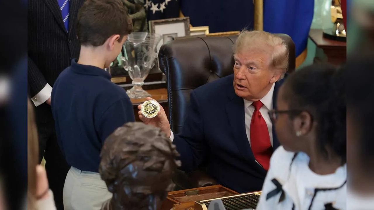 US President Donald Trump presents a boy with a coin on the day he makes an announcement regarding personal investment accounts for children in the Oval Office at the White House in Washington, D.C., US, October 7, 2026. REUTERS/Jonathan Ernst