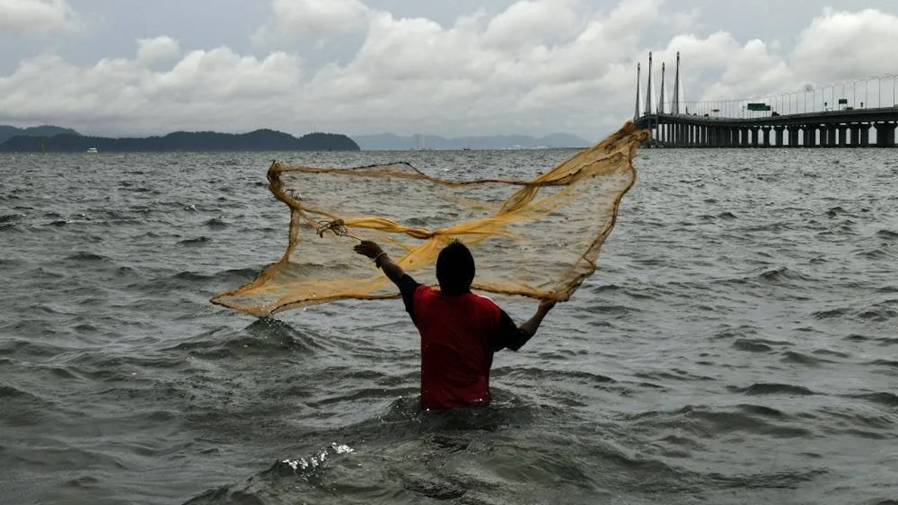 Seorang lelaki menjala ikan di laut yang bergelora berhampiran Jambatan Sultan Abdul Halim Mu’adzam Shah, Georgetown, pada musim Monsun Timur Laut yang kini melanda negara ini.